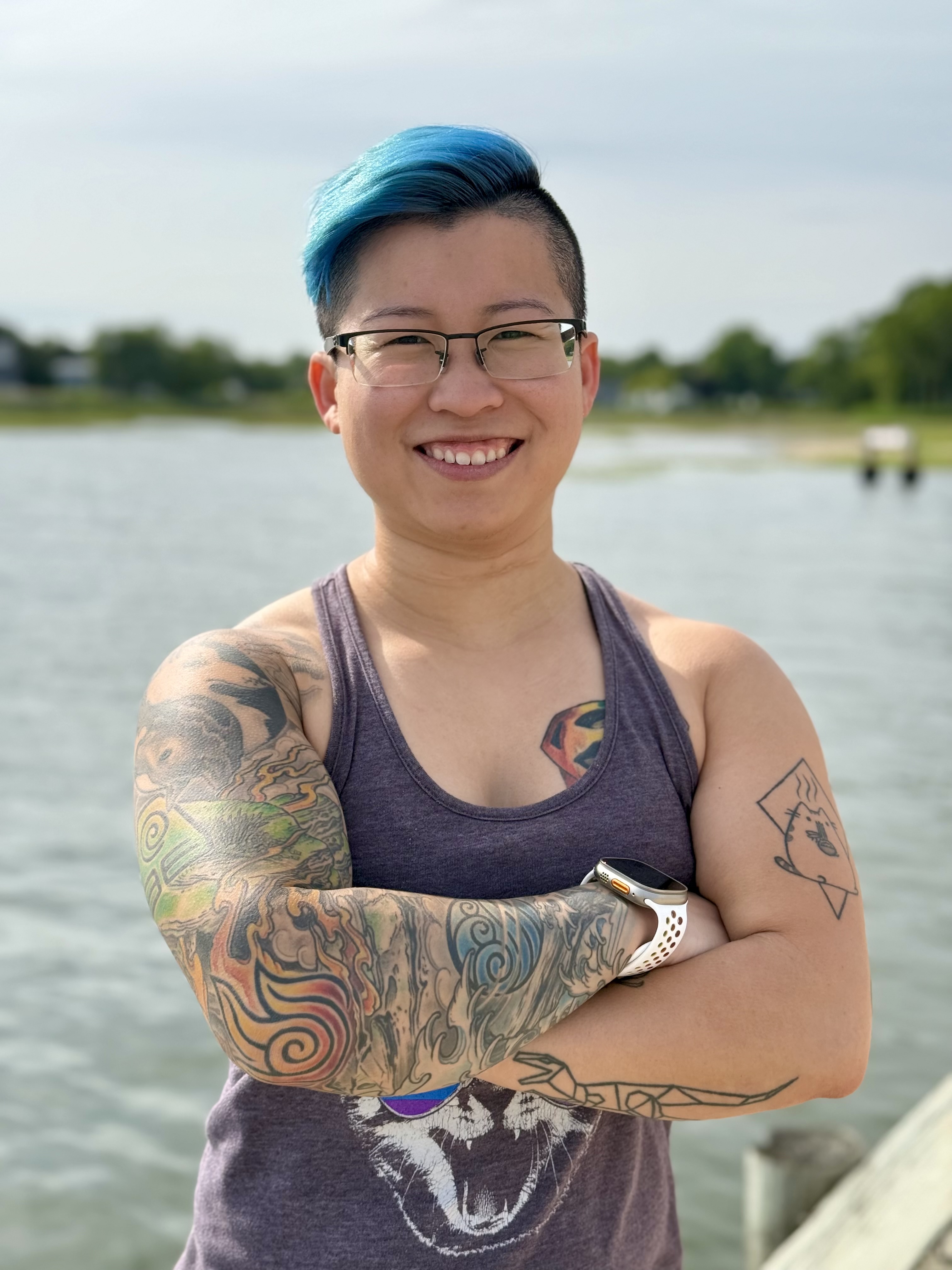 Jin Jin smiling with their arms crossed with the ocean in the background